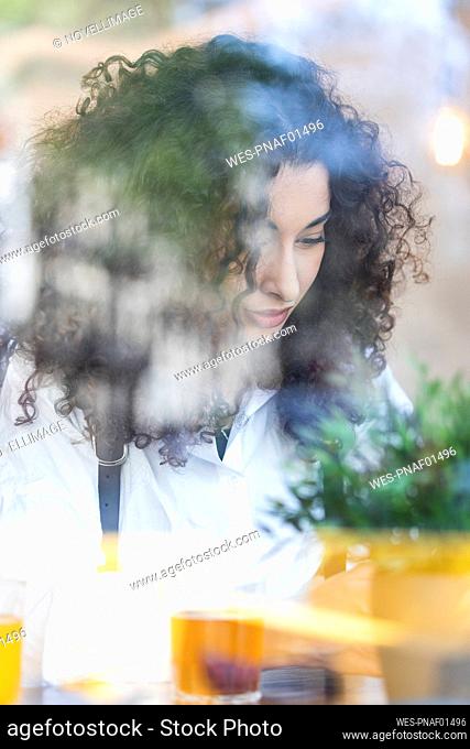 Young woman with curly hair seen through glass at restaurant