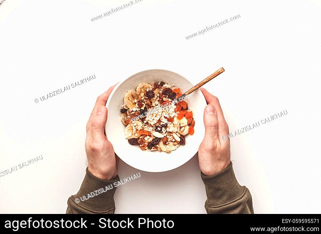 Man holding plate with carbohydrate healthy breakfast. Oatmeal with dried fruits on a white plate. View from above