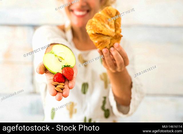 close up and portrait of beautiful woman showing at the camera healthy food like fruit and in the other hand bad alimentation like croissant