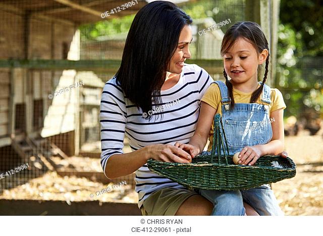 Mother and daughter with basket of eggs outside chicken coop