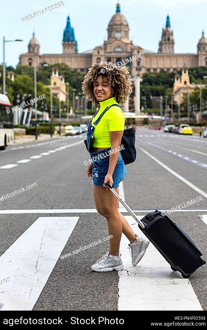 Smiling female wheeling luggage while walking on street at city
