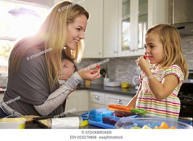 Mum and older daughter eating fruit, while baby sleeps in baby carrier