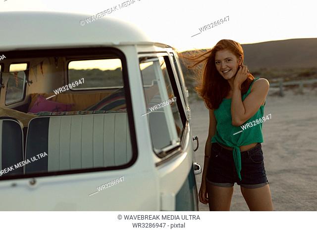 Portrait of beautiful happy Caucasian woman standing near camper van at beach