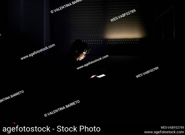 Boy using headphones and digital tablet in his dark room at home