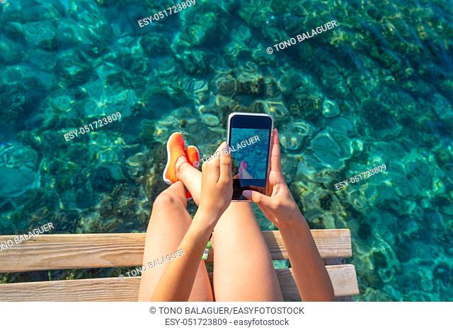 Ibiza girl taking smartphone photos at Portinatx beach pier in Balearic Islands