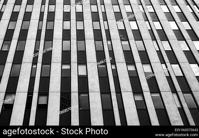 close up perspective detail of tall high rise brutalist style office building with white vertical concrete lines and dark windows