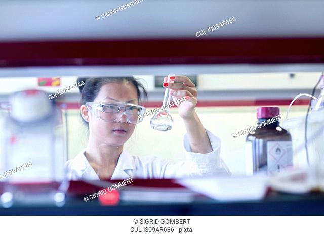 Young female scientist holding up volumetric flask in lab