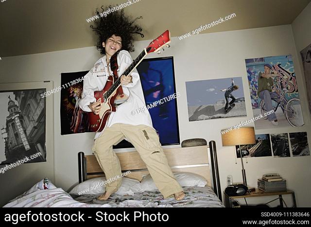 Boy playing guitar and jumping on bed