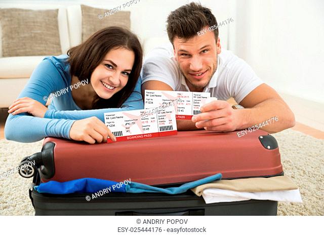 Portrait Of Happy Young Couple Packing Luggage Showing Boarding Pass