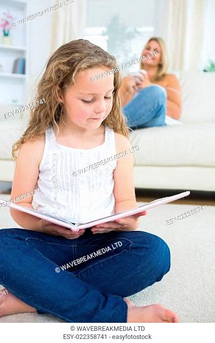 Daughter reading a book while her mother resting on the sofa