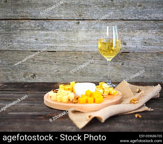 Set of different kind of cheeses with a glass of white wine on the wooden table