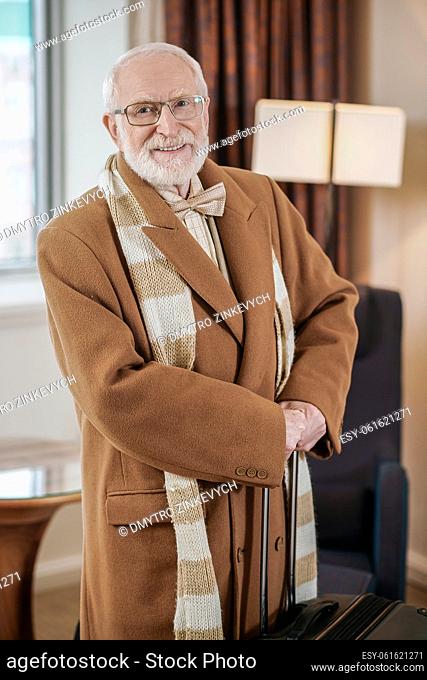 Arrival. Elegant gray-haired man in a brown coat standing in a hotel room