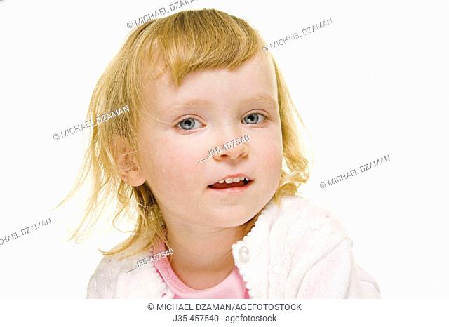 A horizontal image of a three year old girl with blonde hair wearing a white sweater and pink top looks pleased and content
