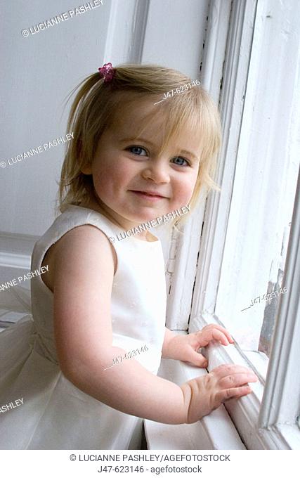 2 year old girl, leaning up against a window smiling into camera