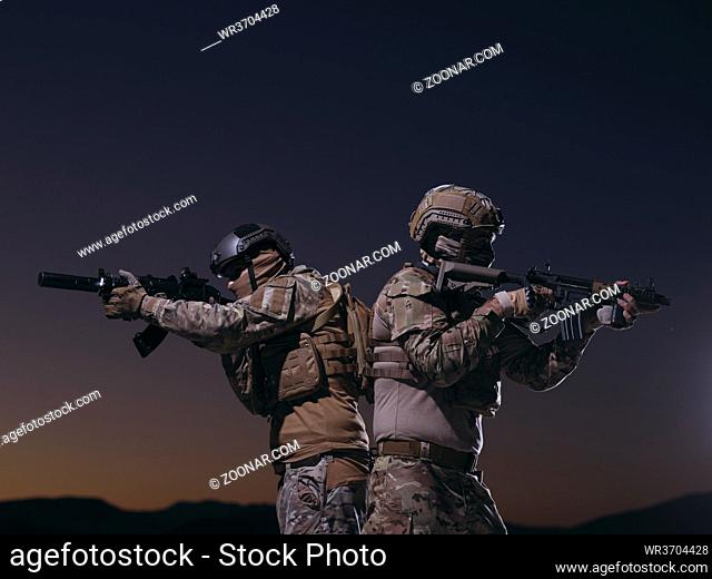 Two heavily armed special forces soldiers in full protective military equipment holding assault rifles and aiming at the targets in night mission
