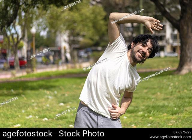 Portrait of handsome attractive mature bearded athletic latin man guy 40s doing stretching exercise, preparing for morning workout in the park
