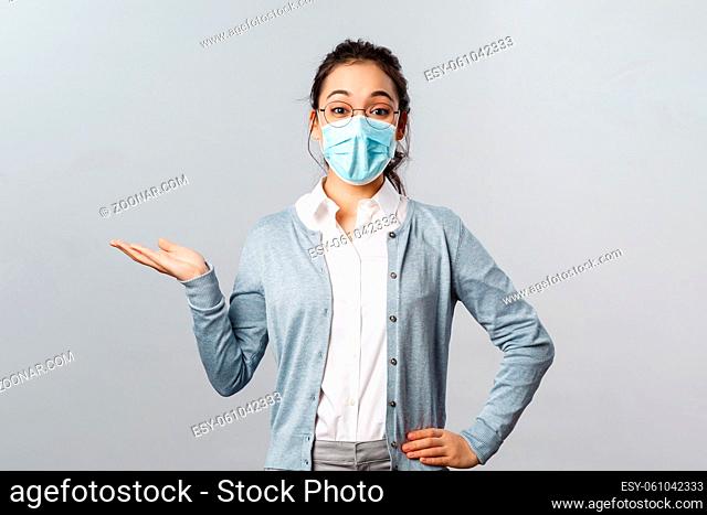 Asian woman in glasses and face mask introduce new company product or banner, pointing, holding promo on hand over left side copy space