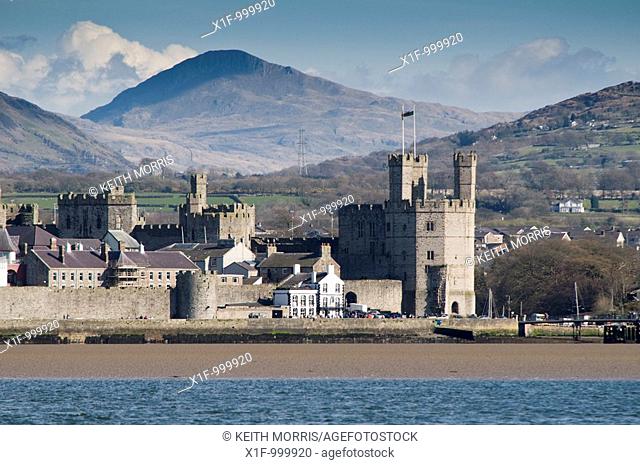Looking accross the Menai Straits to Caernarfon Castle and the mountains of snowdonia national park, gwynedd north wales UK