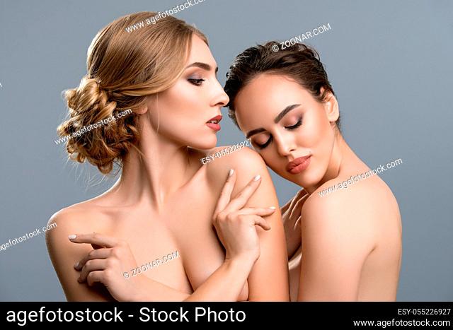 Two nude females keeping eyes closed and gently touching each other against gray background