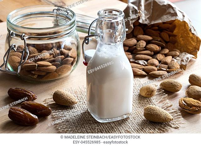 A bottle of almond milk with whole (unshelled) and shelled almonds and dates
