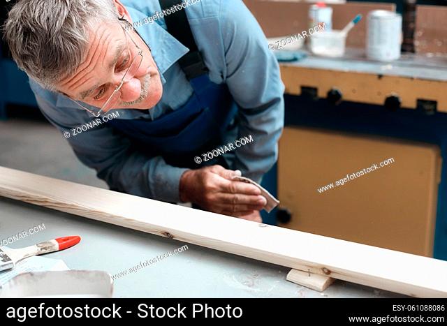 Carpenter's work in the carpentry shop. An elderly male cabinetmaker carefully examines a wooden board. Preparation of the product for painting