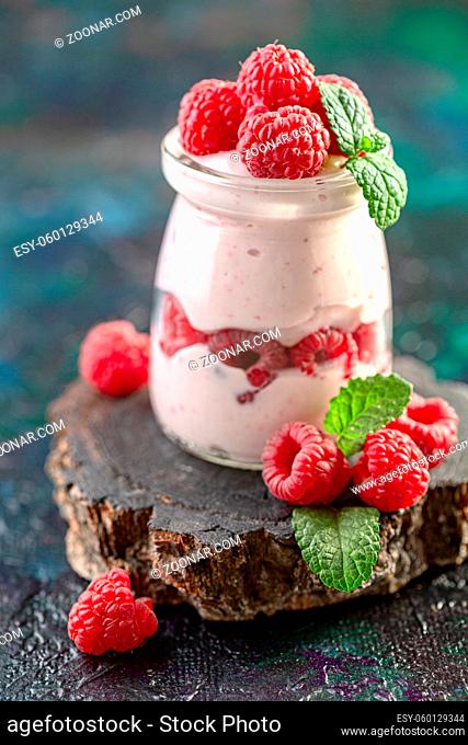 Homemade berry yogurt decorated mint leaves and raspberry in glass jar on wooden stand. Diet and healthy breakfast