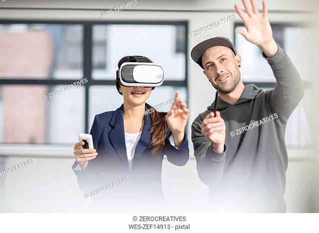 Man instructiong businesswoman wearing VR glasses in office