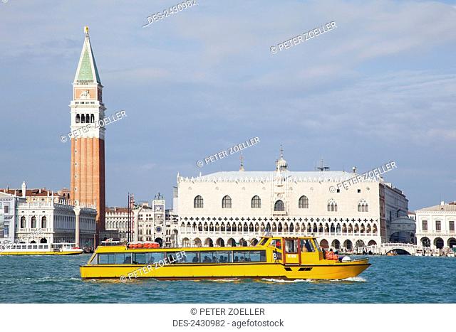 A yellow tour boat in the water with a view of Venice from San Giorgio Maggiore; Venice, Italy