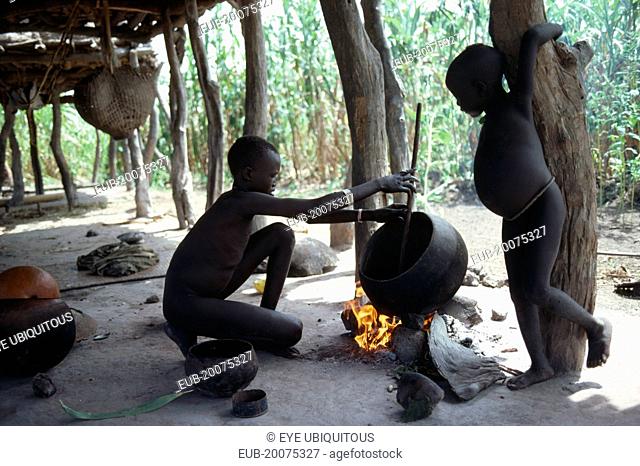 Dinka children cooking over open fire beneath house raised above ground level