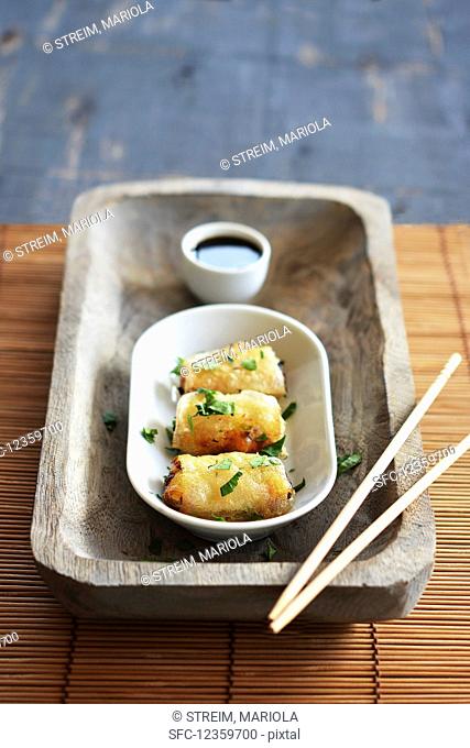 Spring rolls in a bowl with soy sauce on a rustic tray with chopsticks