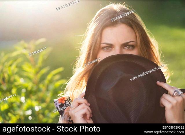 Closeup portrait of beautiful girl hiding her face behind hat in sunny day. Horizontally
