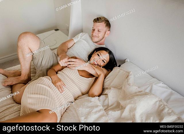 Smiling woman lying with male partner over bed in bedroom
