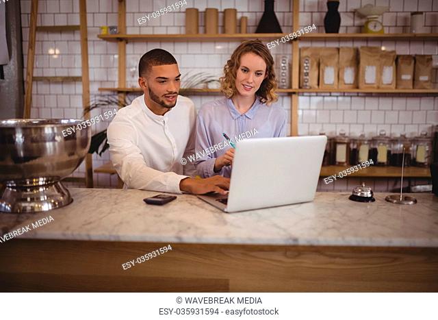 Male owner and young waitress using laptop while sitting at counter