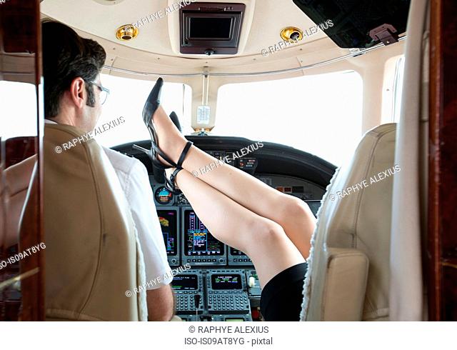 Rear view of female pilot with feet up in cockpit of private jet