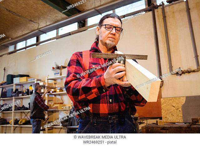 Carpenter looking if the wood plank is straight in his workshop