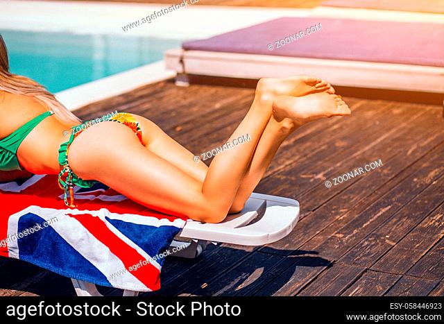 Woman's legs in green bikini sunbathing on the beach lounger near swimming pool during tropical travelling or vacation. Summer scene concept