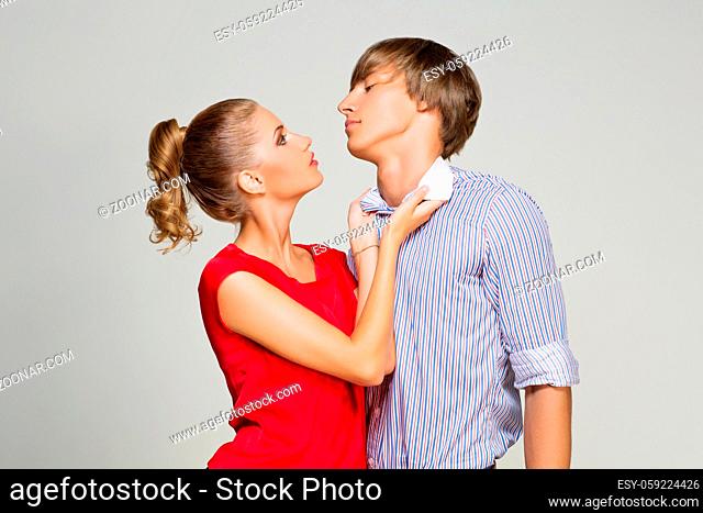 Beautiful couple argueing. Woman holding young man shirl collar. Over grey background