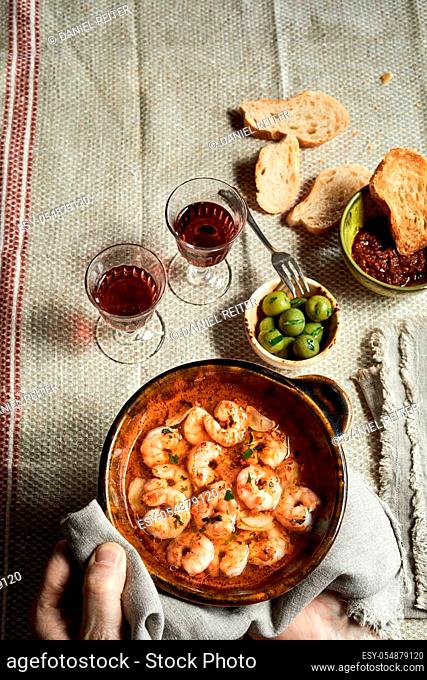 Gourmet dish of Spanish scampi with garlic sauce being placed on a table set with glasses of red wine by the hand of the chef from overhead