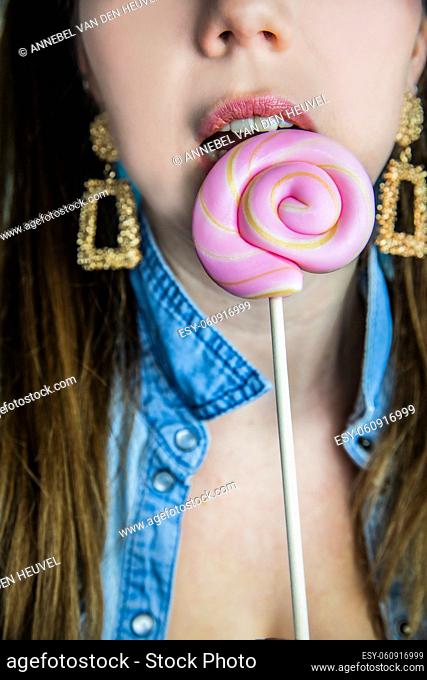 Portrait of a beautiful girl with colorful pink twirl lollipop hard candy on blue background, sweets, sugar and unhealthy food concept beauty