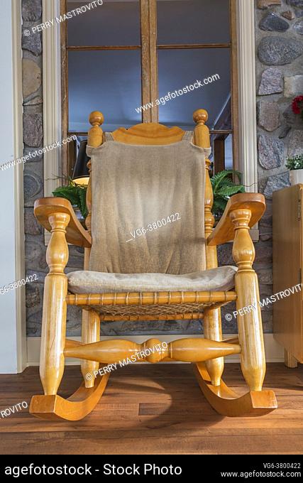 Canadiana style pine wood rocking chair with large turned posts against original stone wall with window in extension with floating wood floor at back of old...