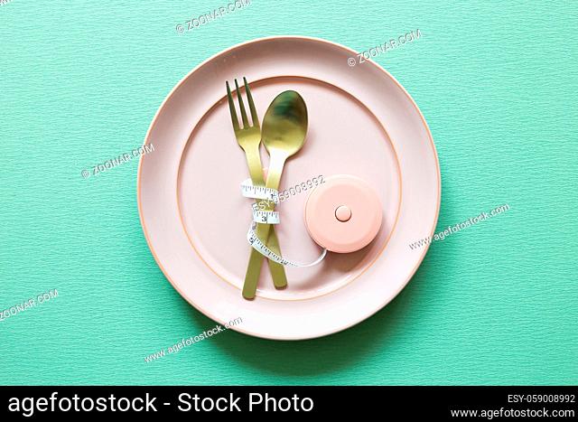 Plate and fork, spoon with measuring tape on green background. Diet concept