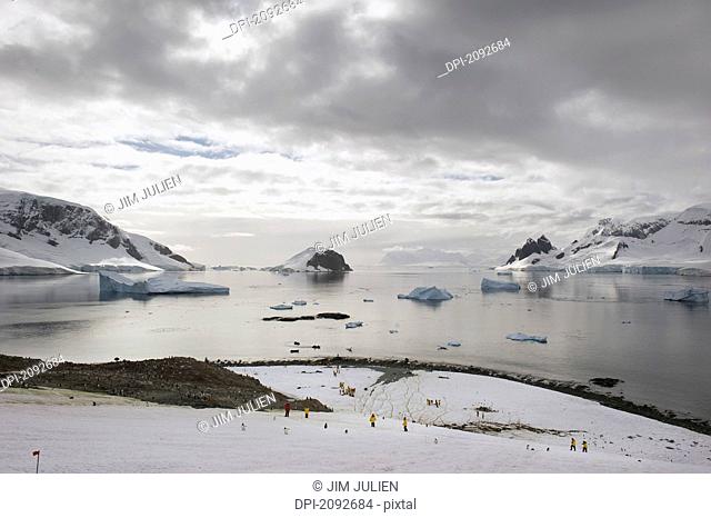 People standing on the ice with icebergs and mountains along the coastline, antarctica