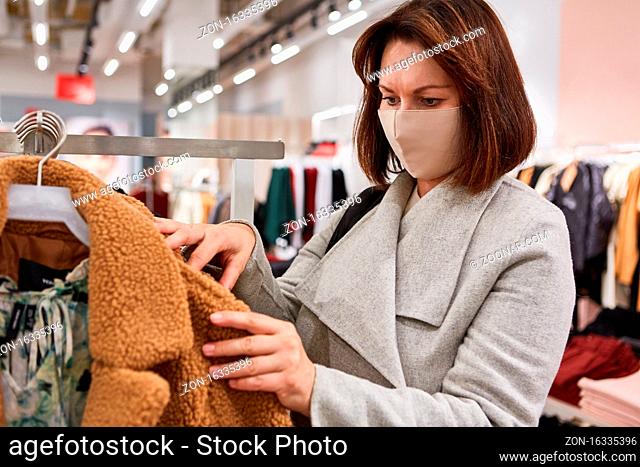 Frau als Kundin mit Gesichtsmaske wegen Covid-19 Pandemie in einer Mode Boutique