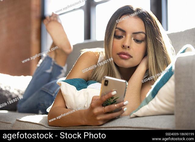 Woman laying on couch using smart phone at home