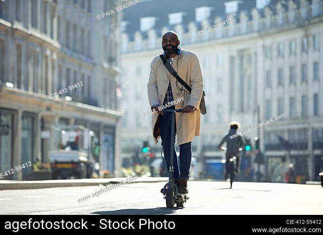 Businessman riding electric push scooter on sunny city street