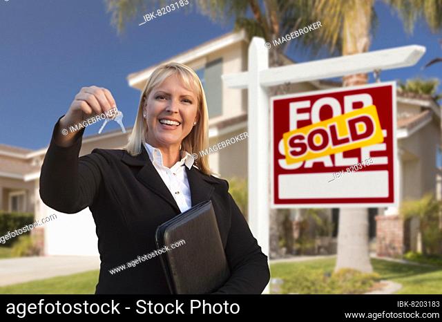 Female real estate agent handing over the house keys in front of a beautiful new home and real estate sign