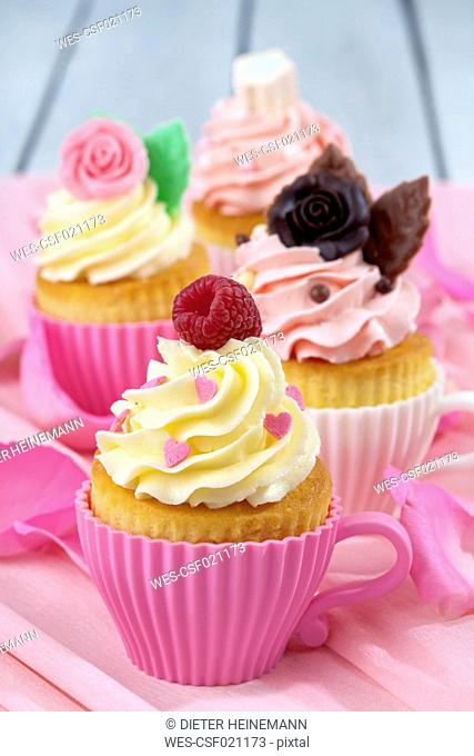Four baking dishes formed like cups with decorated cupcakes on pink crepe paper