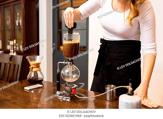 equipment, coffee shop, people and technology concept - close up of woman stirring coffee grounds in siphon coffeemaker top vessel at cafe bar or restaurant...