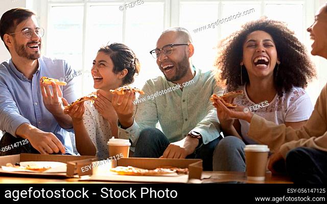 Horizontal wide image cheery multi-ethnic friends students eat tasty pizza seated on couch indoors, gathered together chatting laughing enjoy talk and ordered...