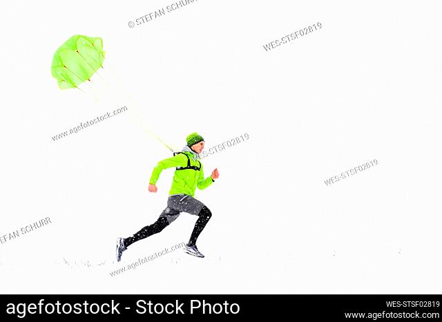 Male athlete with parachute running on snow during winter